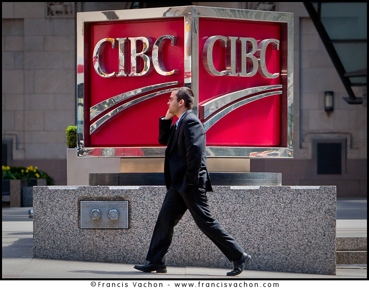 A man talking on his cell phone walks by a CIBC logo in Toronto financial district